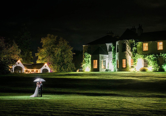 Newlyweds under umbrella on grounds of Aberdeen Wedding Venue Logie Country House